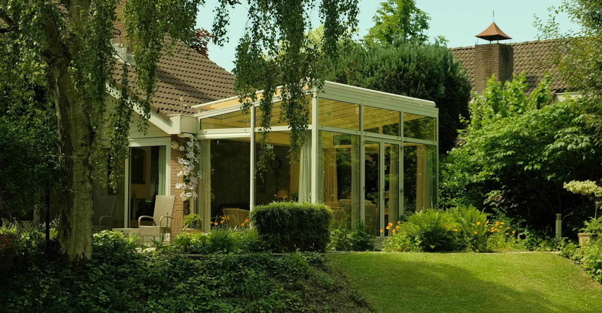 Modern glass sunroom attached to a house, surrounded by trees